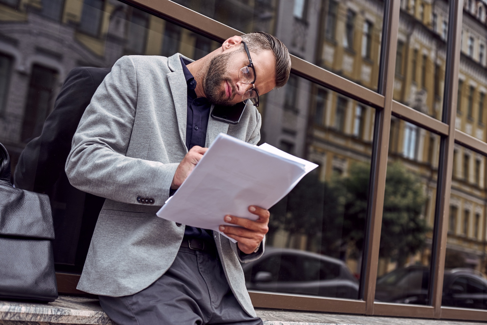 Business communications. Young businessman standing leaning on wall on the city street talking on